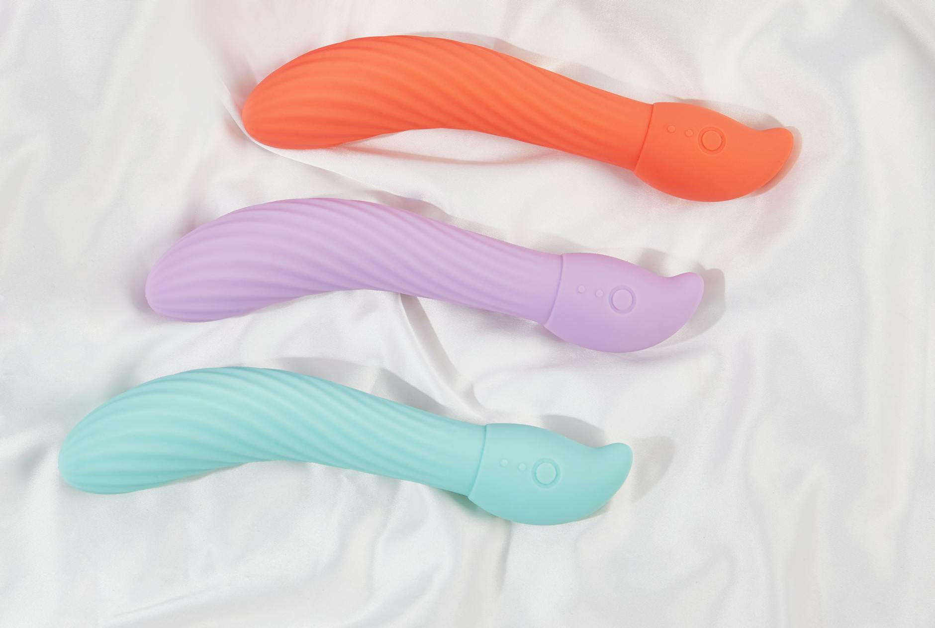 Three colorful clitoral vibrators arranged on white fabric, highlighting smooth texture and design variety