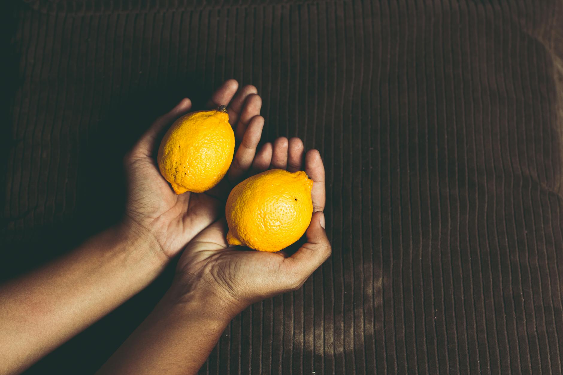 Fresh lemons held in cupped hands on a brown surface, symbolizing new beginnings