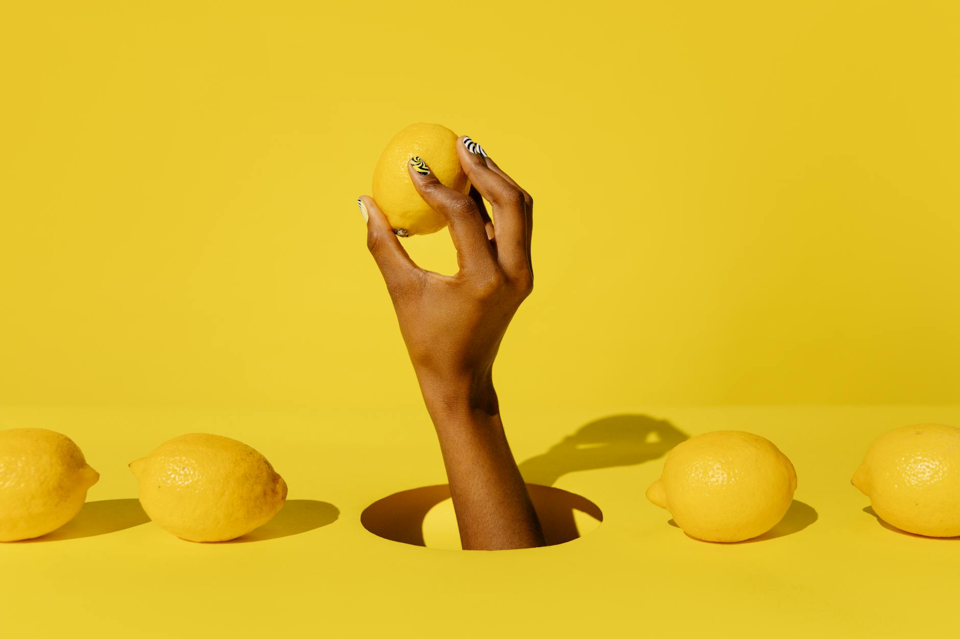 A hand holding a fresh lemon against a yellow background, symbolizing renewal and freshness after hormonal changes