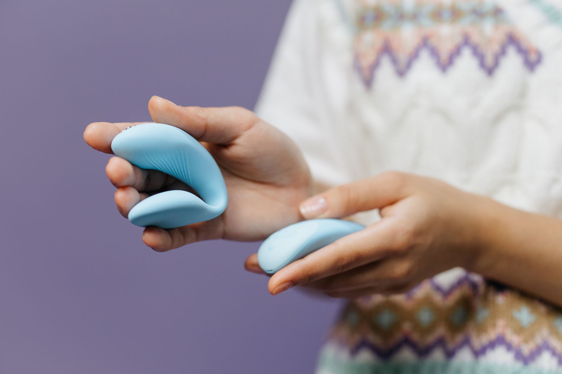 Close-up of hands holding a sleek blue vibrator against a purple background, showing gentle intimate touch