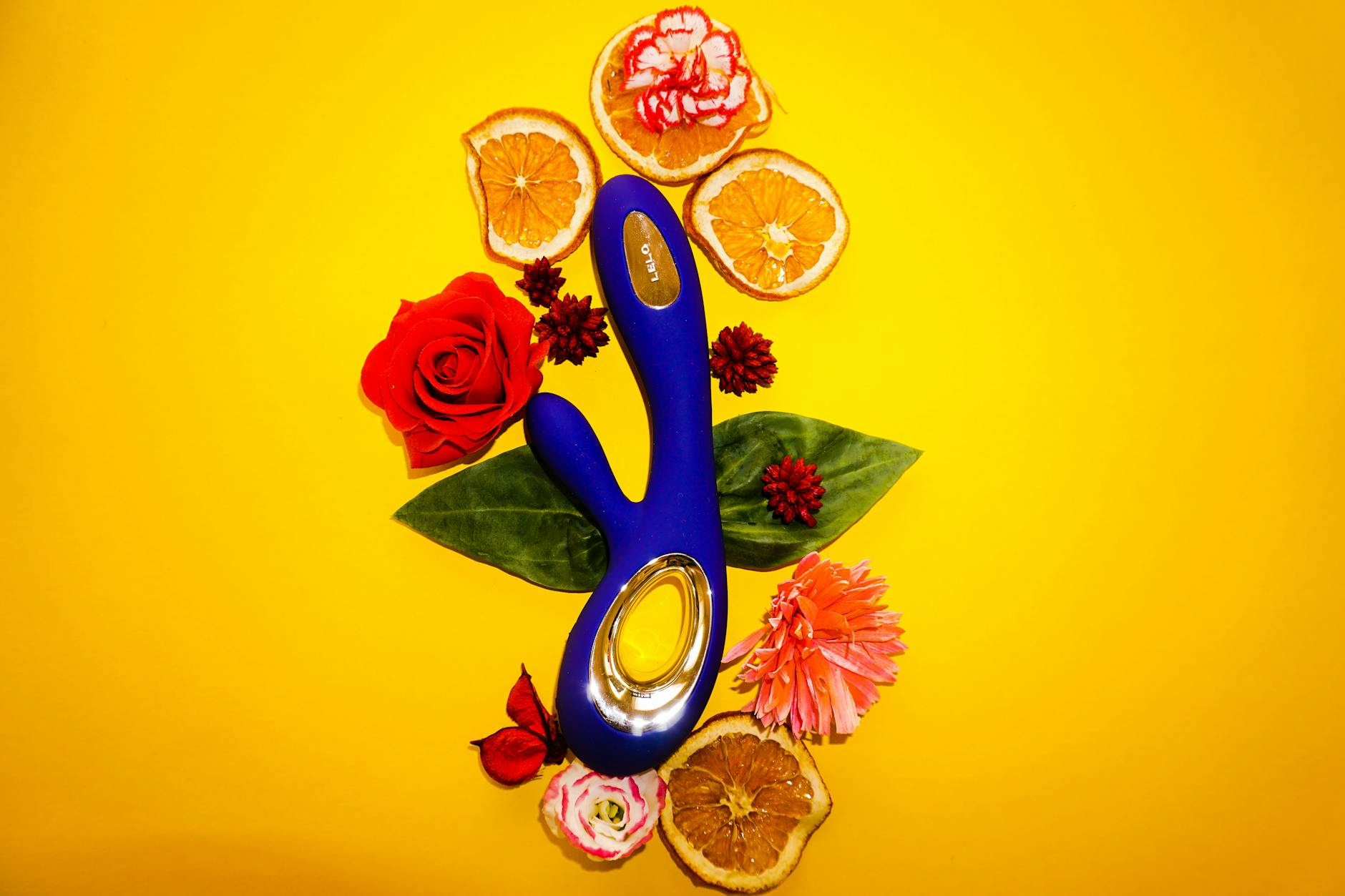 A blue lemon clitoral vibrator surrounded by flowers and orange slices on a yellow background